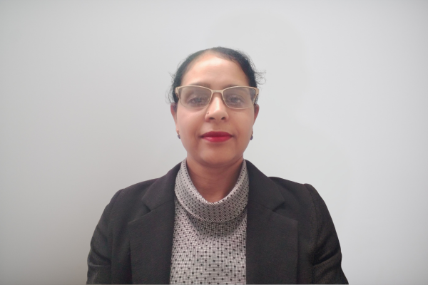 Professional head-and-shoulders portrait of a woman in a dark blazer and patterned blouse, wearing glasses against a light gray background.