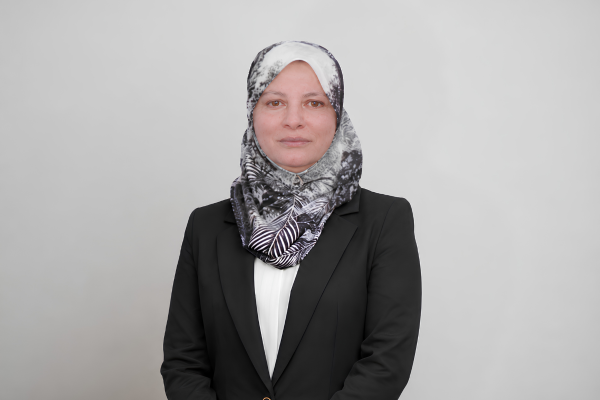 Professional portrait of a woman wearing a black blazer and patterned hijab, facing the camera with a neutral expression.